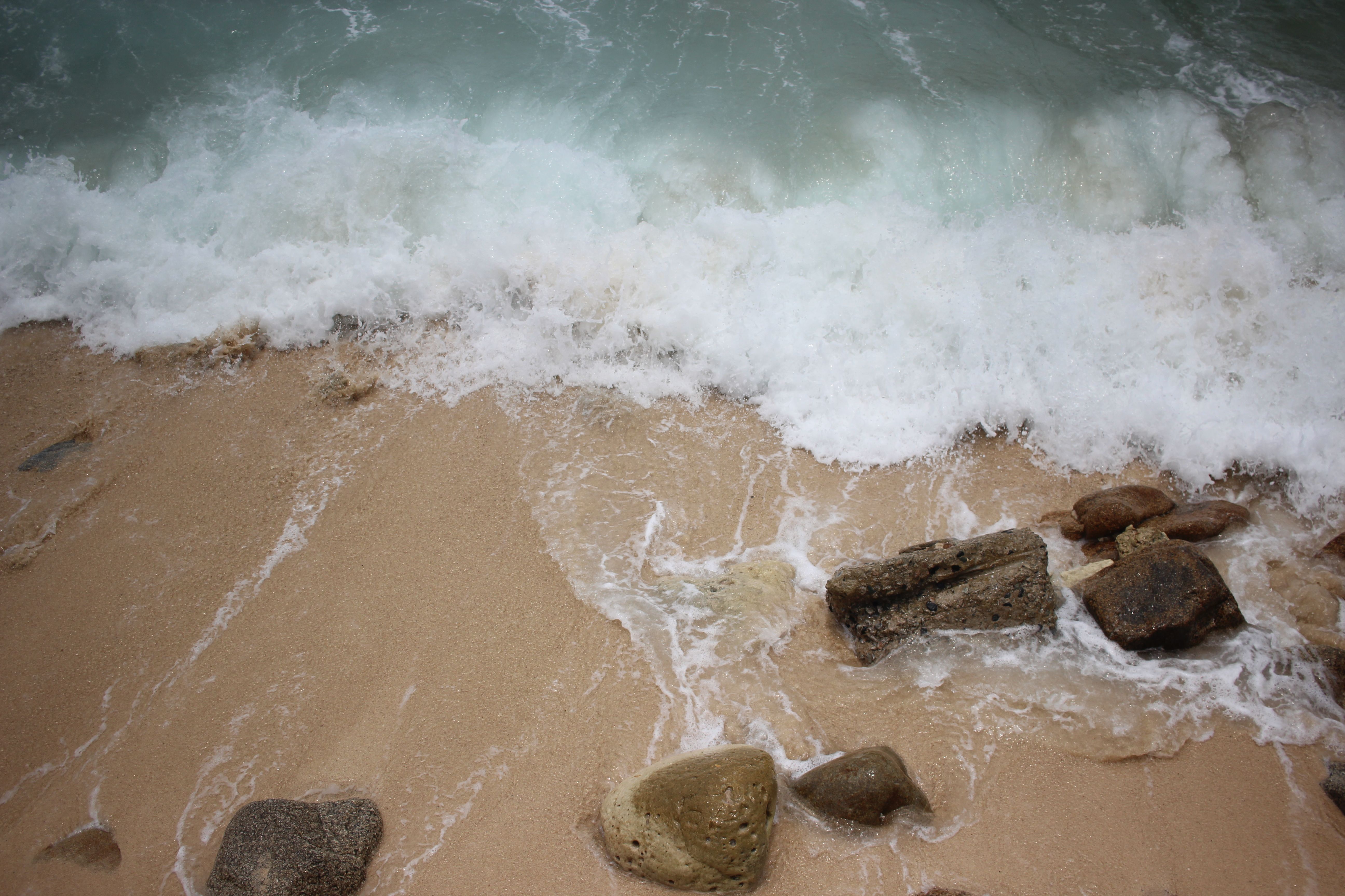 Serene image of waves gently crashing on a sandy beach with rocks, ideal for relaxation themes.
