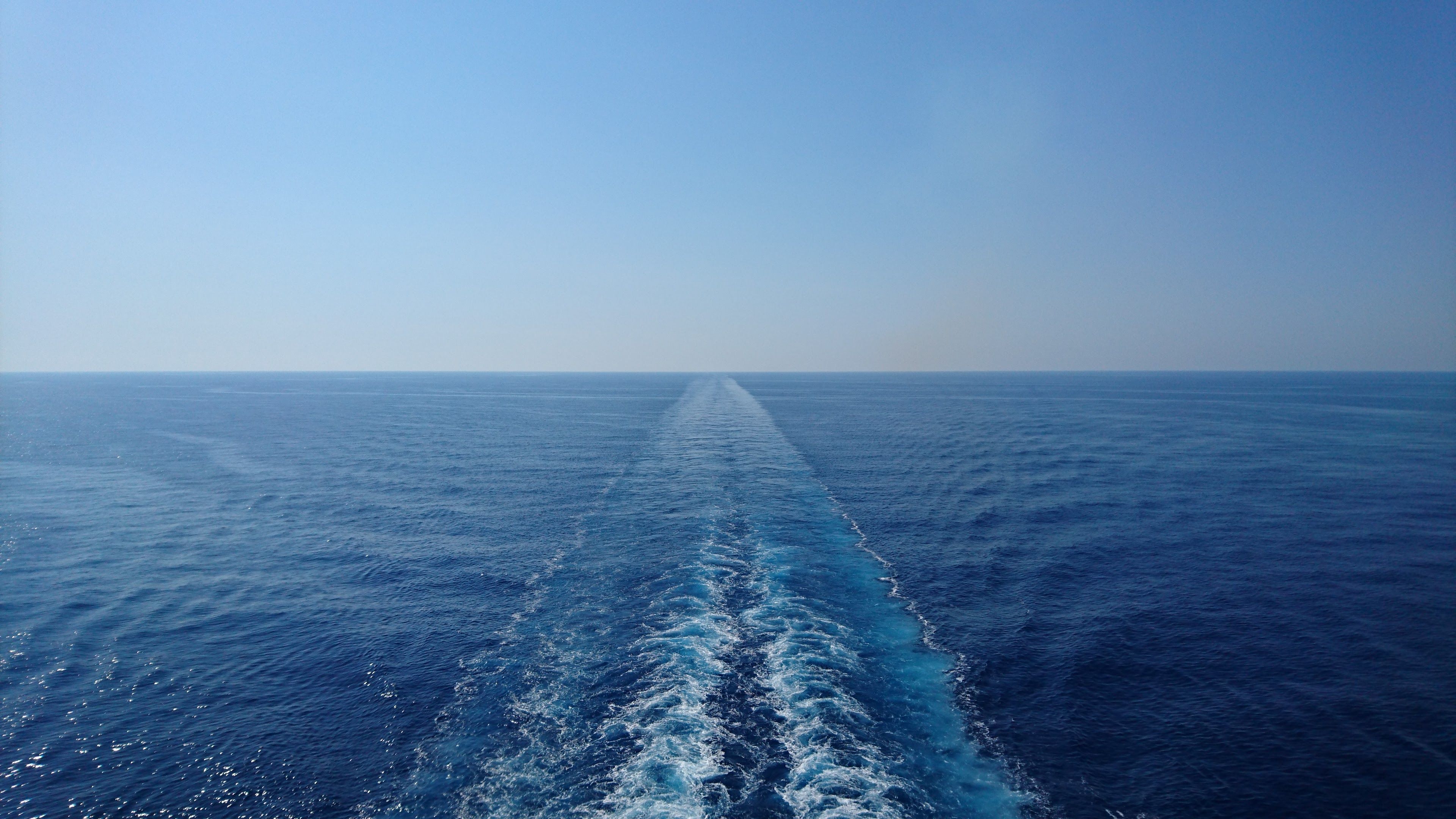 A serene ocean scene with a ship's wake trailing under a clear blue sky, showcasing tranquility and vastness.
